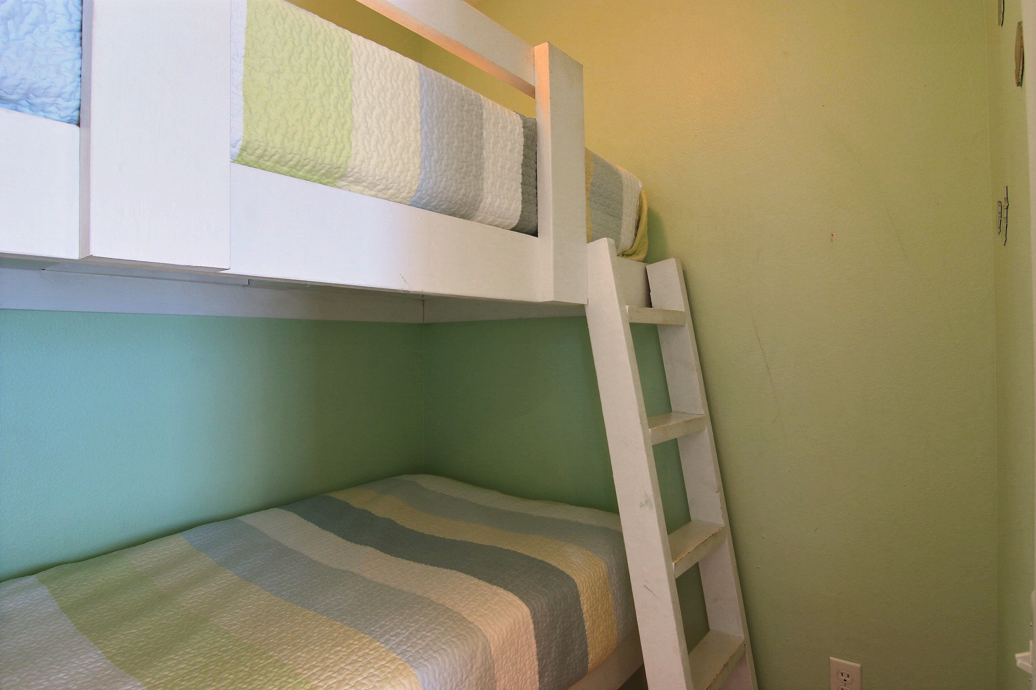 A bunk bed with a ladder, a single bed below, and a green wall.