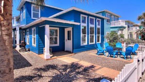 Una casa de dos pisos con fachada azul, un porche con sillas azules y una cerca blanca de piquetes.