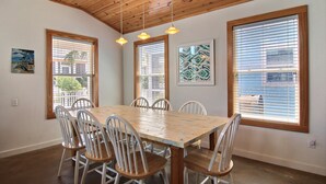 Un comedor con una mesa y sillas de madera, ventanas amplias con persianas e iluminación colgante.