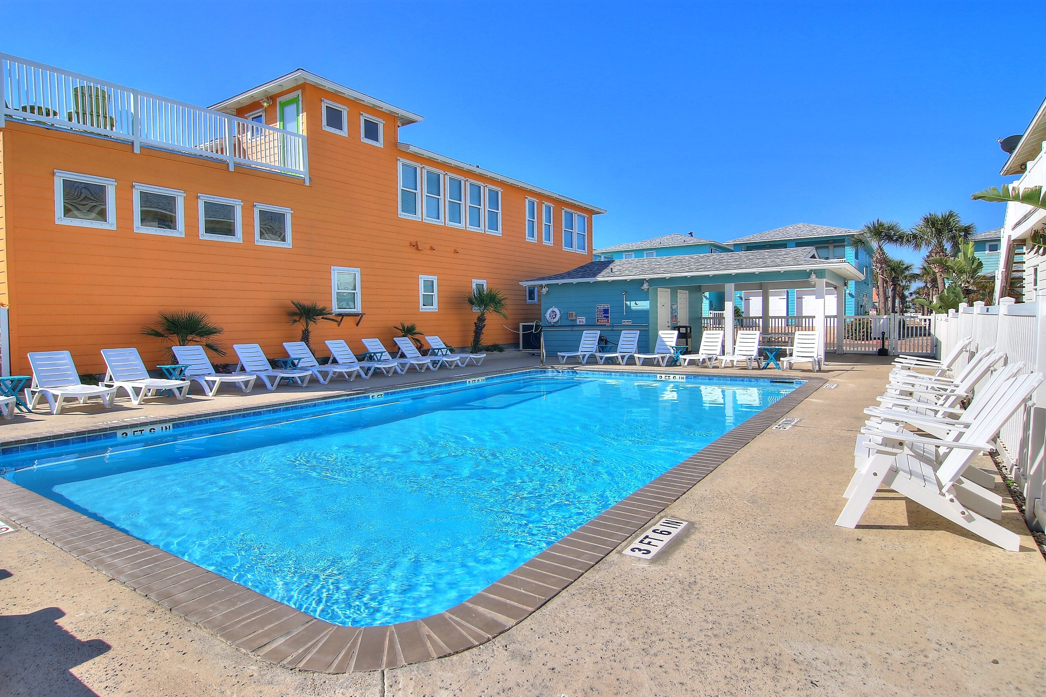A swimming pool with lounge chairs, a building with a balcony, and palm trees.