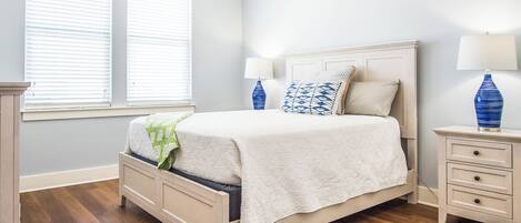 A bedroom with a bed, bedside tables, and a window with blinds.