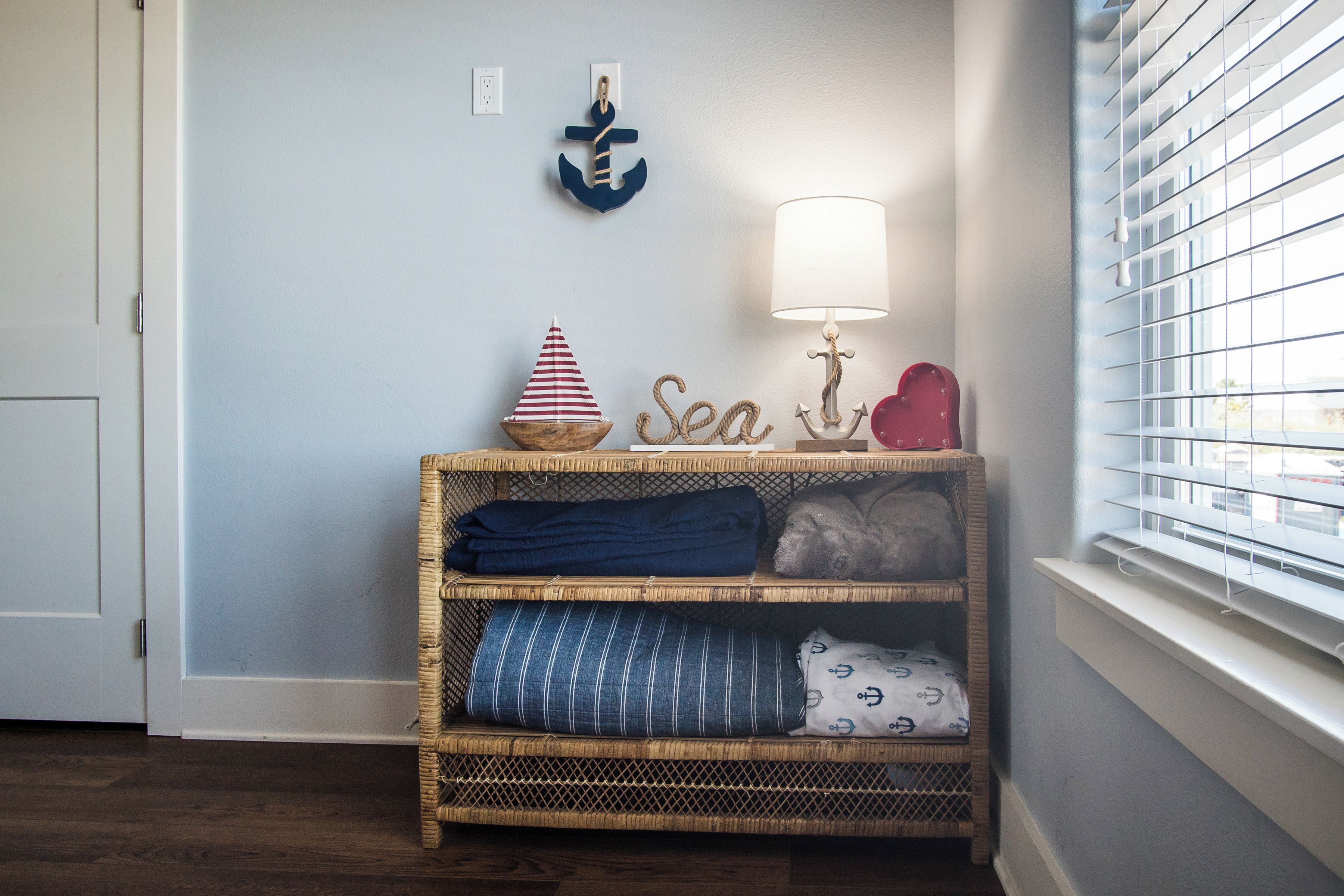 A corner with a wicker shelf holding folded blankets, a small ship decoration, and a wall-mounted anchor.