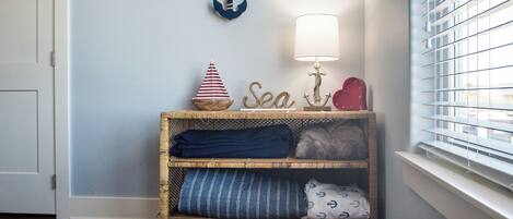A corner with a wicker shelf holding folded blankets, a small ship decoration, and a wall-mounted anchor.