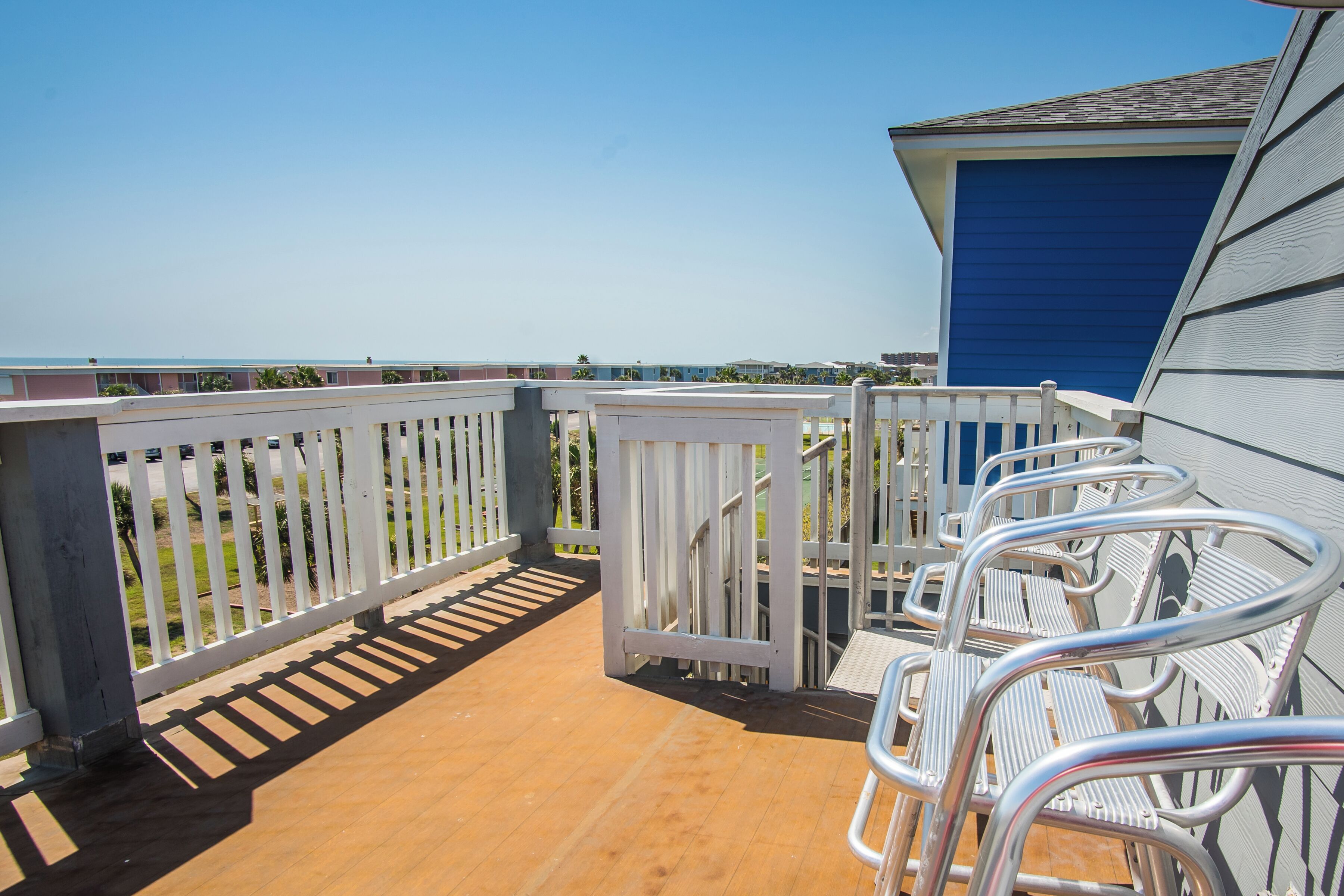 A balcony with metal chairs and a white railing overlooking a beach.