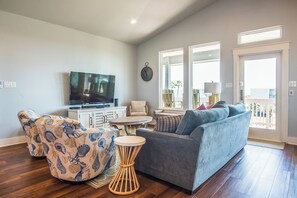 A living room with a grey sofa, patterned armchairs, a TV, and a dining table. - Mer Sea Azul by Silver Sands Vacation Rentals (Port Aransas)