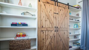 Quarto com porta de celeiro deslizante de madeira, prateleiras brancas com diversos objetos e uma cesta trançada.