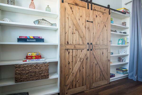A room with a wooden sliding barn door, white shelves with various items, and a woven basket. - Mer Sea Azul by Silver Sands Vacation Rentals (Port Aransas)