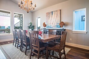A dining area with a wooden table and chairs, a chandelier, and a large abstract painting on the wall. - Mer Sea Azul by Silver Sands Vacation Rentals (Port Aransas)