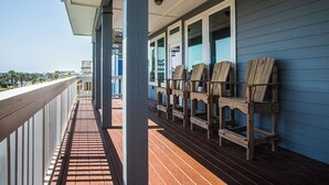 Um deck de madeira com cadeiras, um corrimão e vista para o oceano.