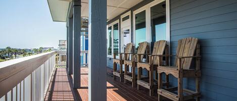 A wooden deck with chairs, a railing, and a view of the ocean.
