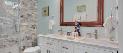 Un baño con cabina de ducha de vidrio, un inodoro blanco, un tocador con un espejo grande y una figura decorativa en el lavabo.