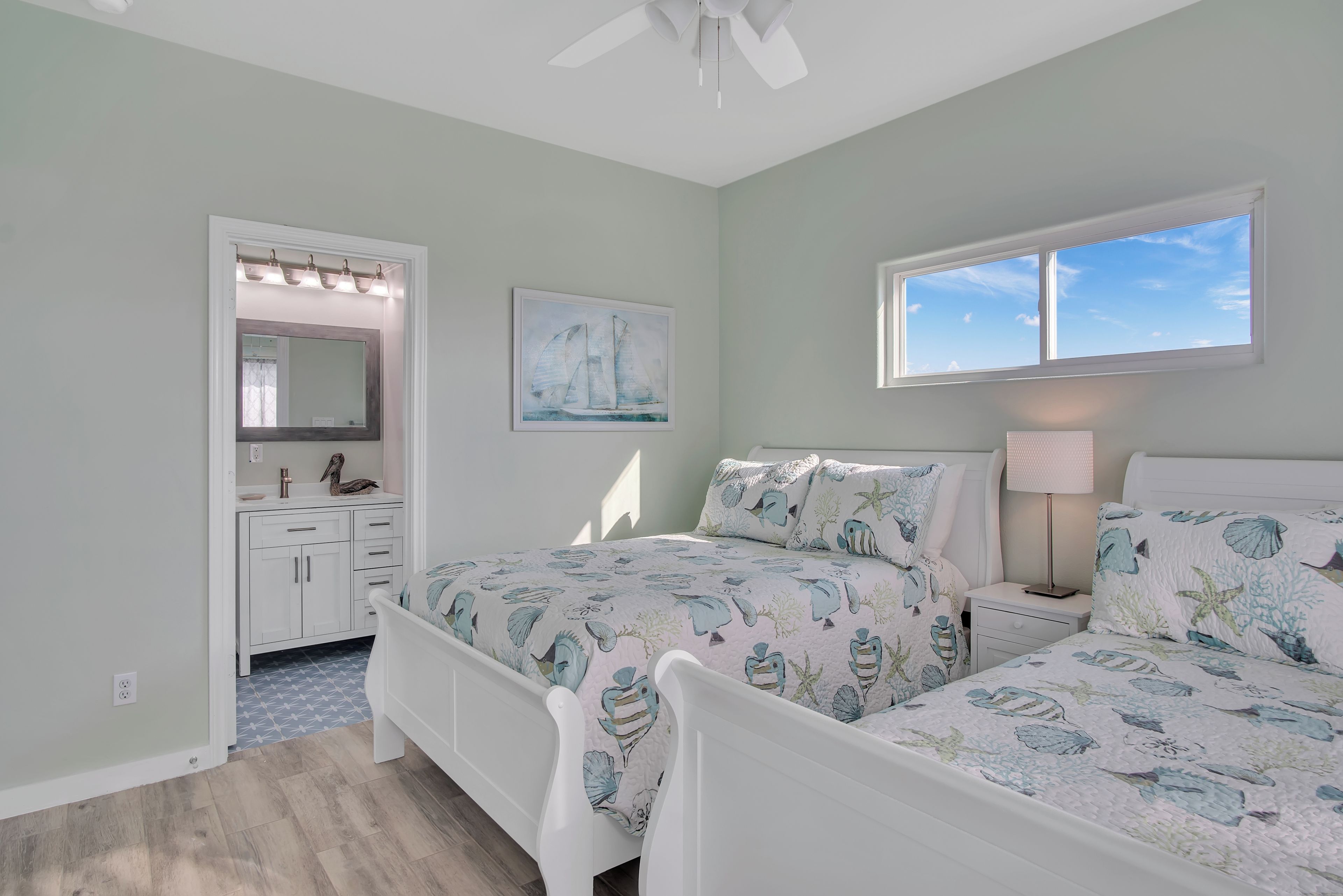 A bedroom with a bed, bedside table, lamp, and a window with a view of the sky.