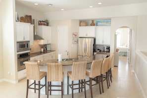 A modern kitchen with white cabinets, stainless steel appliances, and a central island with bar stools. - Oceans 10 by Silver Sands Vacation Rentals (Port Aransas)