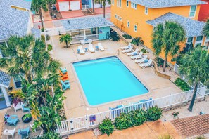 An aerial view of a pool area with lounge chairs, a small building, and palm trees. - Oceans 10 by Silver Sands Vacation Rentals (Port Aransas)