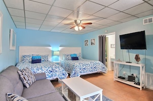 A hotel room with two beds, a sofa, a TV, and a ceiling fan.