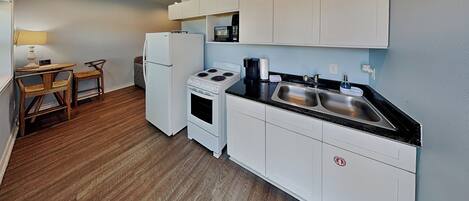 A compact kitchen with white cabinets, a stove, a refrigerator, a microwave, and a sink.