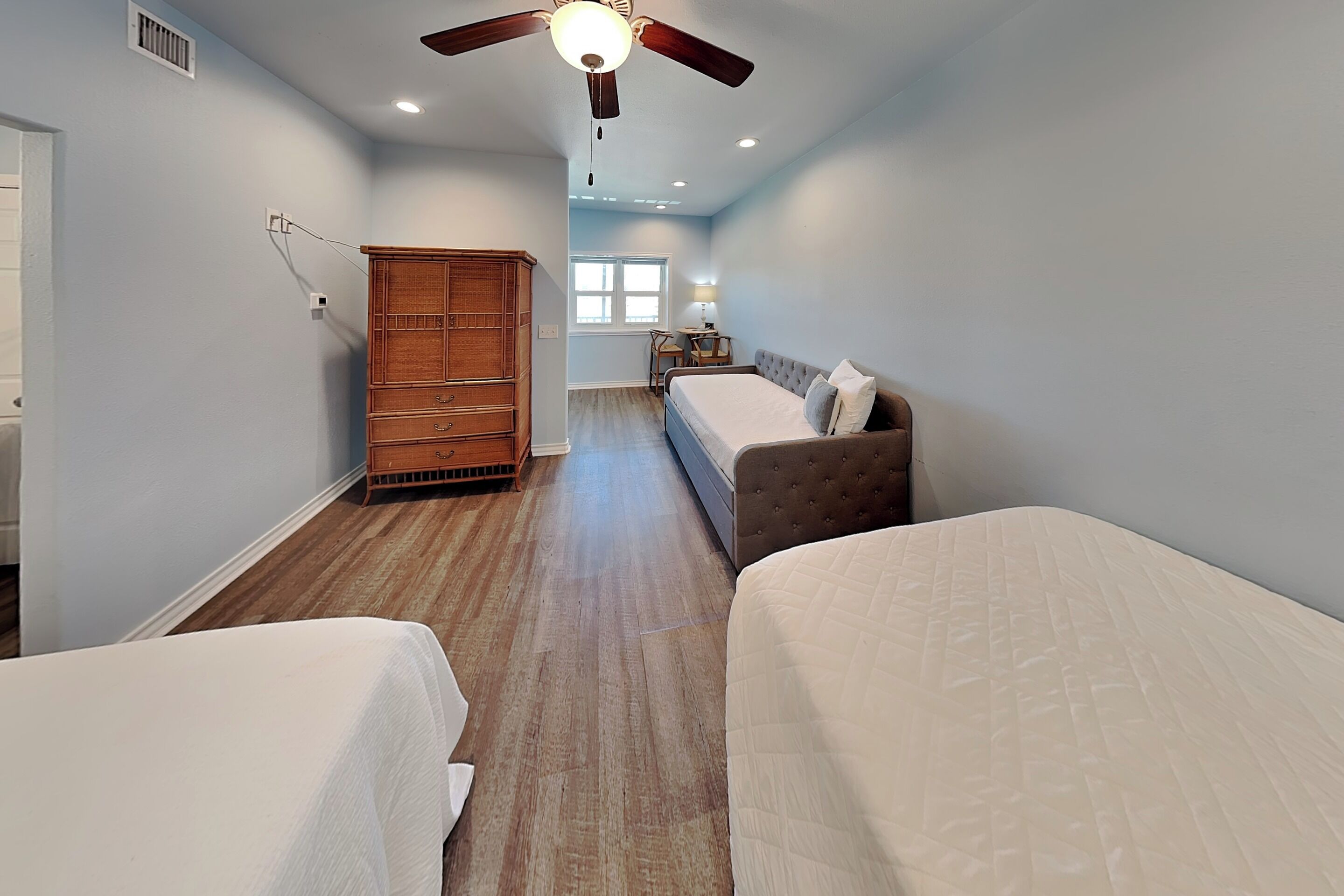 A hotel room with two beds, a wardrobe, a ceiling fan, and a window.