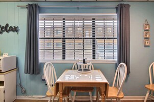 A dining area with a table and chairs, a window with blinds, a small refrigerator, and a wall-mounted sign.