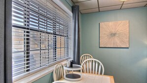A dining area with a table and chairs, a window with blinds, and a wall-mounted abstract art piece.