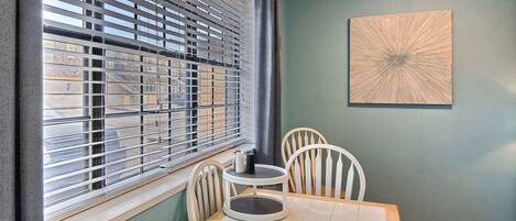 Un comedor con mesa y sillas, una ventana con persianas y una obra de arte abstracta colgada en la pared.
