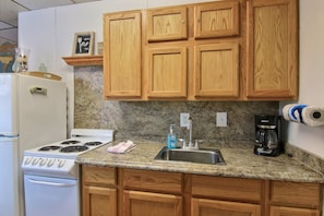 A kitchen with wooden cabinets, a white stove, a granite countertop, a sink, and a coffee maker. - On the Half Shell by Silver Sands Vacation Rentals (Port Aransas)