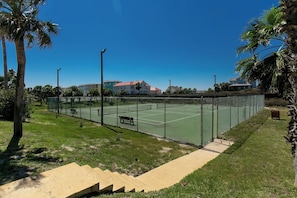 Una cancha de tenis con valla, bancos y una escalera que lleva a la cancha.