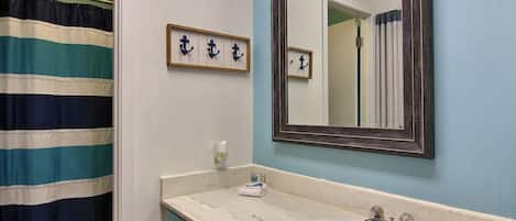 A bathroom with a striped shower curtain, a sink with a mirror above it, and a towel rack with towels.
