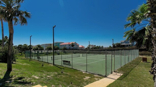 A tennis court with a fence, benches, and a staircase leading to the court.