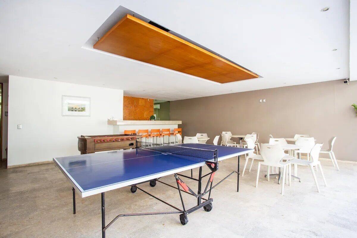 Een tafeltennistafel in een kamer met witte stoelen en een houten tafel met oranje stoelen.