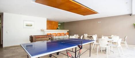 Una mesa de ping pong en una habitación con sillas blancas y una mesa de madera con sillas anaranjadas.