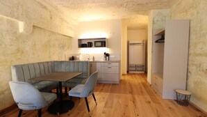 A compact living space with a dining area featuring a gray bench and a small table, a kitchenette with a microwave and coffee maker, and a walk-in closet. - Das Fischer Boardinghouse KF (Kaufbeuren)