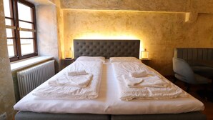 A double bed with white linens and towels, a grey upholstered bench, a wall-mounted headboard, and two bedside lamps. - Das Fischer Boardinghouse KF (Kaufbeuren)