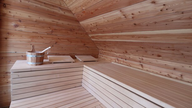 A wooden sauna with benches and a wooden bucket. - Das Fischer Boardinghouse KF (Kaufbeuren)