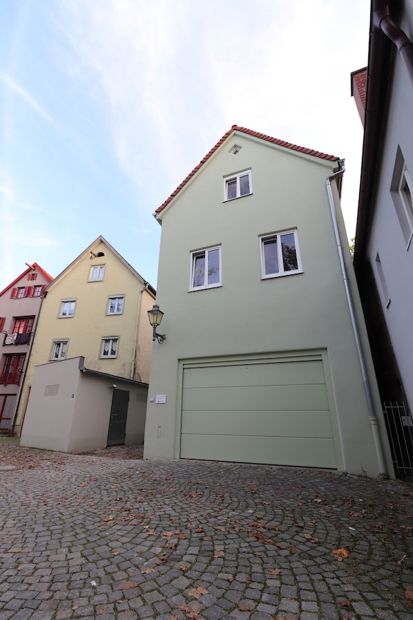 A building with a light green facade, a red-tiled roof, and a garage door. - Das Fischer Boardinghouse KF (Kaufbeuren)