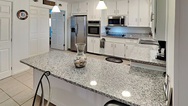 A modern kitchen with white cabinets, granite countertops, stainless steel appliances, and pendant lighting. - Paradise Retreat by Silver Sands Vacation Rentals (Port Aransas)