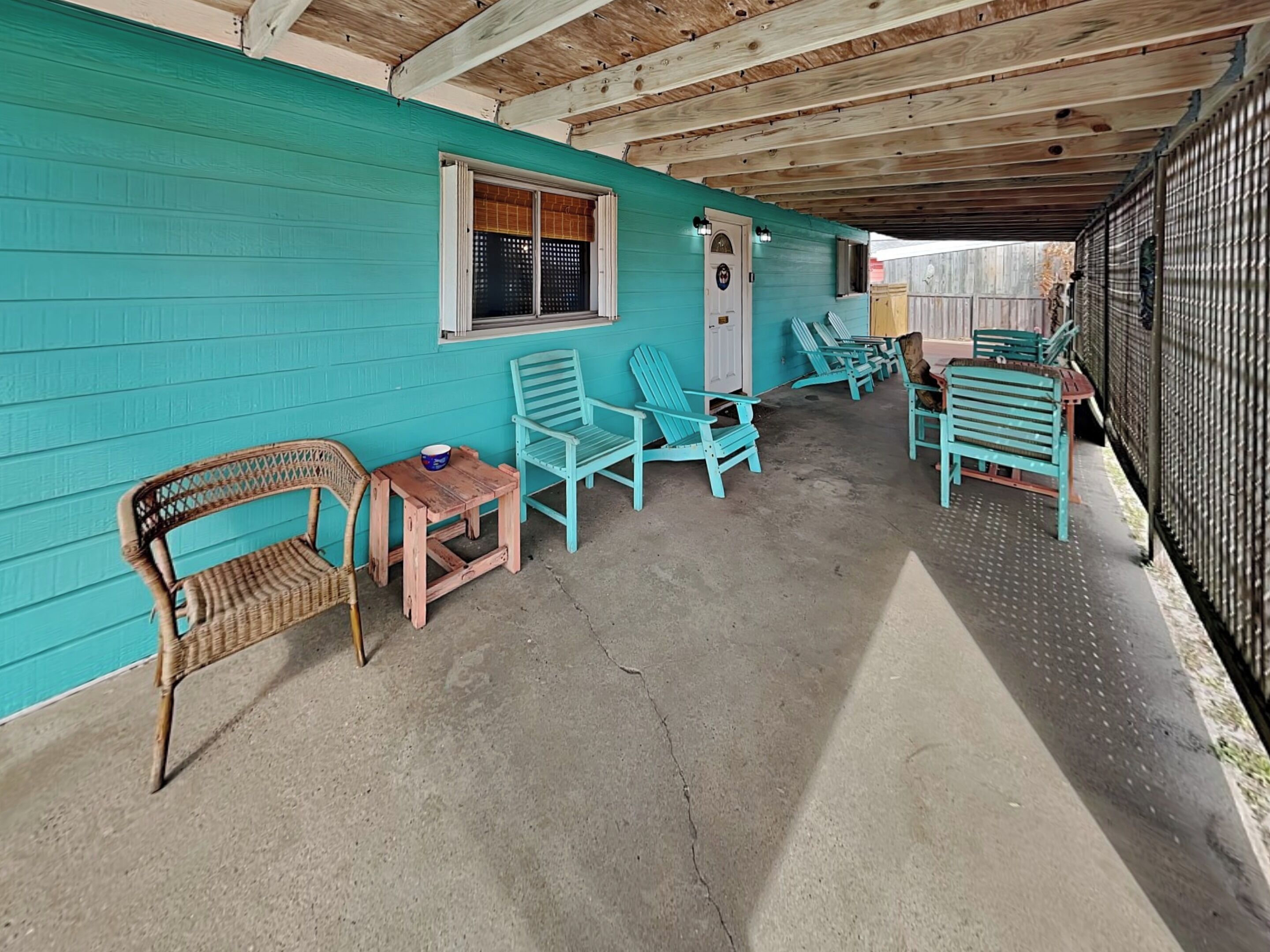Un patio cubierto con paredes turquesas, vigas de madera en el techo y varios sillones Adirondack.