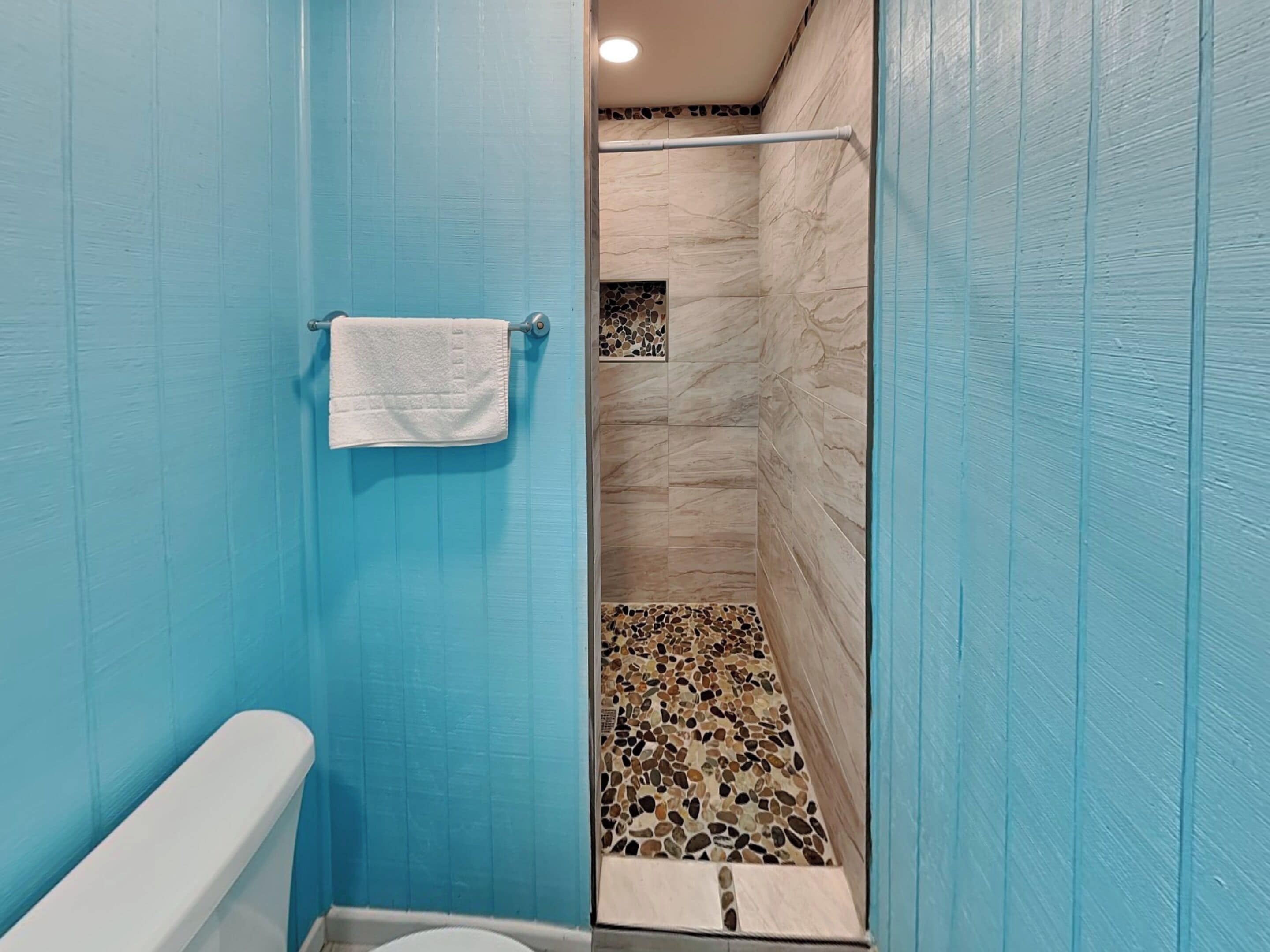 A bathroom with blue walls, a white toilet, and a shower area with a mosaic floor.