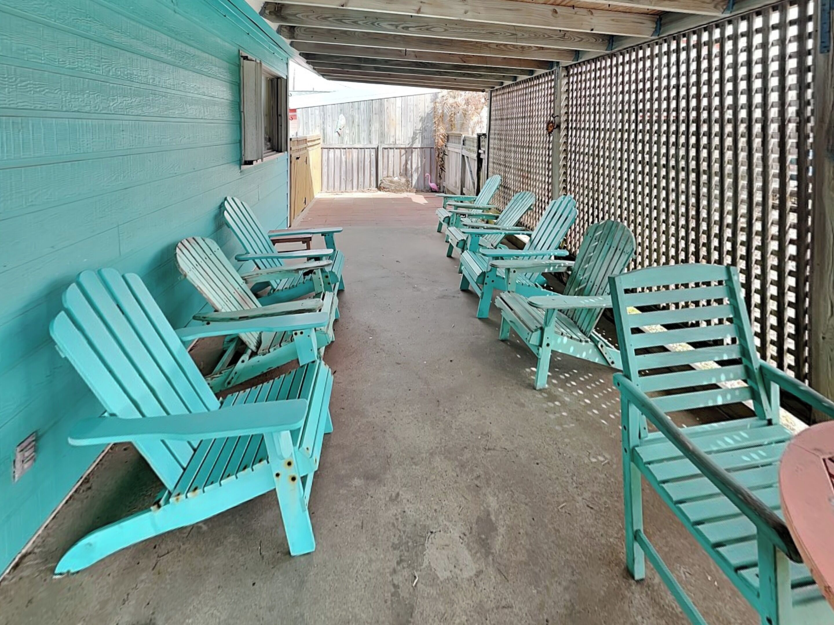 A covered outdoor seating area with turquoise Adirondack chairs arranged in rows.