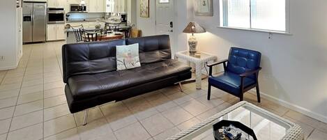 Una sala de estar con un sofá de cuero negro, un sillón azul y una mesa de centro de vidrio.