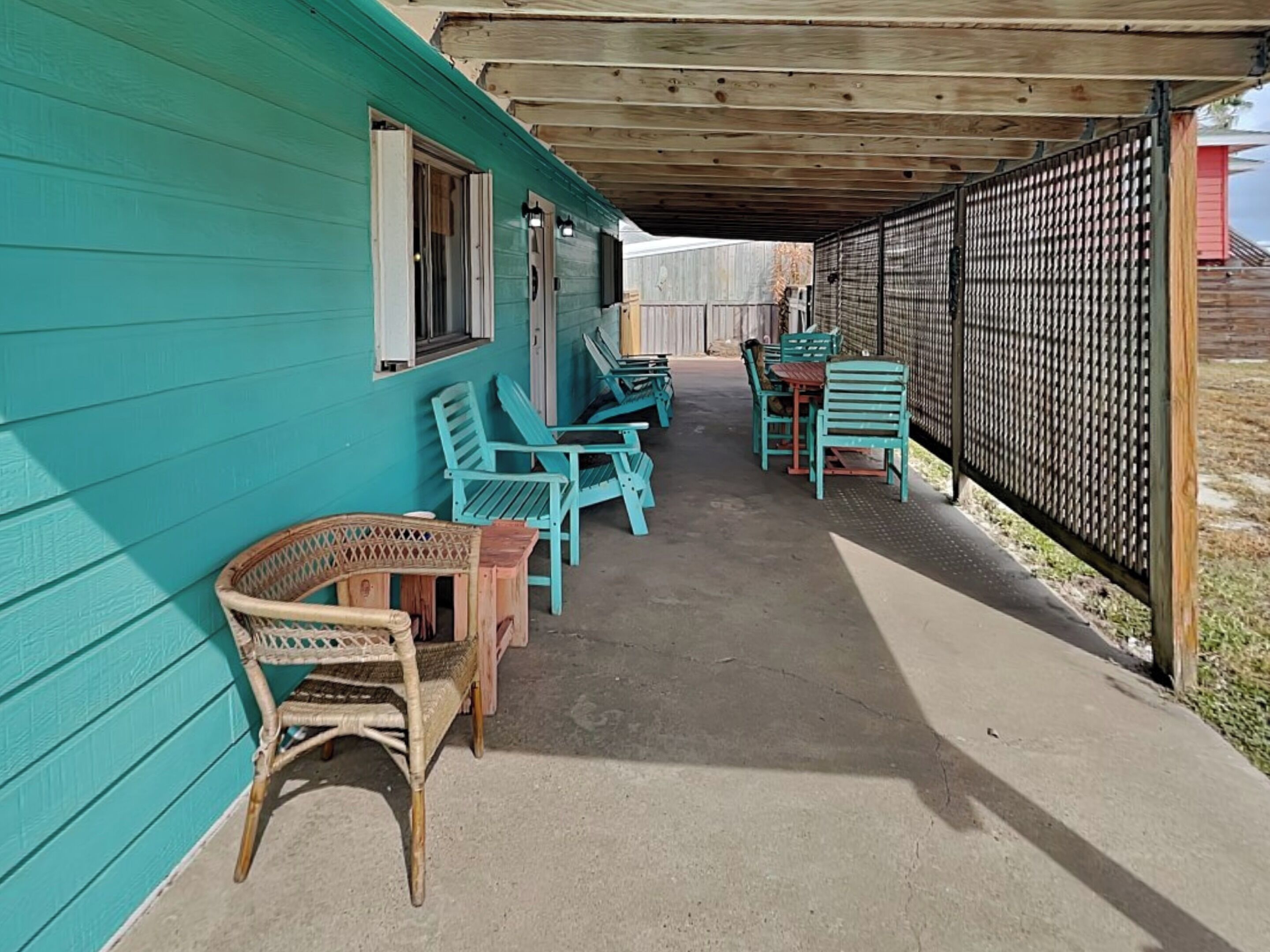 A covered outdoor area with turquoise walls, wicker furniture, and a concrete floor.