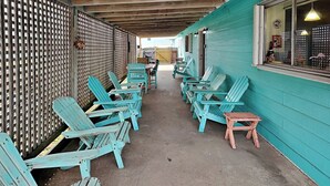 A covered outdoor seating area with rows of Adirondack chairs and a small wooden table. - Paradise Retreat by Silver Sands Vacation Rentals (Port Aransas)