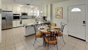 A modern kitchen with white cabinets, a stainless steel refrigerator, a built-in oven, and a dining area with a round table and chairs. - Paradise Retreat by Silver Sands Vacation Rentals (Port Aransas)