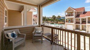 A balcony with wicker chairs and a view of a residential area with multiple buildings. - Port A Good Time by Silver Sands Vacation Rentals (Port Aransas)