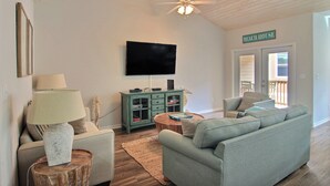 A living room with a teal sofa, a wooden coffee table, a lamp, a TV, and a ceiling fan. - Port A Good Time by Silver Sands Vacation Rentals (Port Aransas)