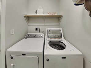 A laundry room with two white washing machines and a shelf above labeled 'LAUNDRY'. - Port A Good Time by Silver Sands Vacation Rentals (Port Aransas)