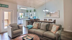 A living room with a sofa, armchair, and coffee table. There is a dining area with a table and chairs, and a kitchen in the background. - Port A Good Time by Silver Sands Vacation Rentals (Port Aransas)