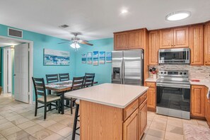A kitchen with wooden cabinets, stainless steel appliances, and a tiled floor. - Pawsitively Paradise by Silver Sands Vacation Rentals (Port Aransas)