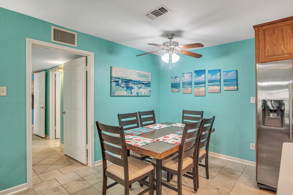 A dining area with a wooden table and chairs, a ceiling fan, and a refrigerator.