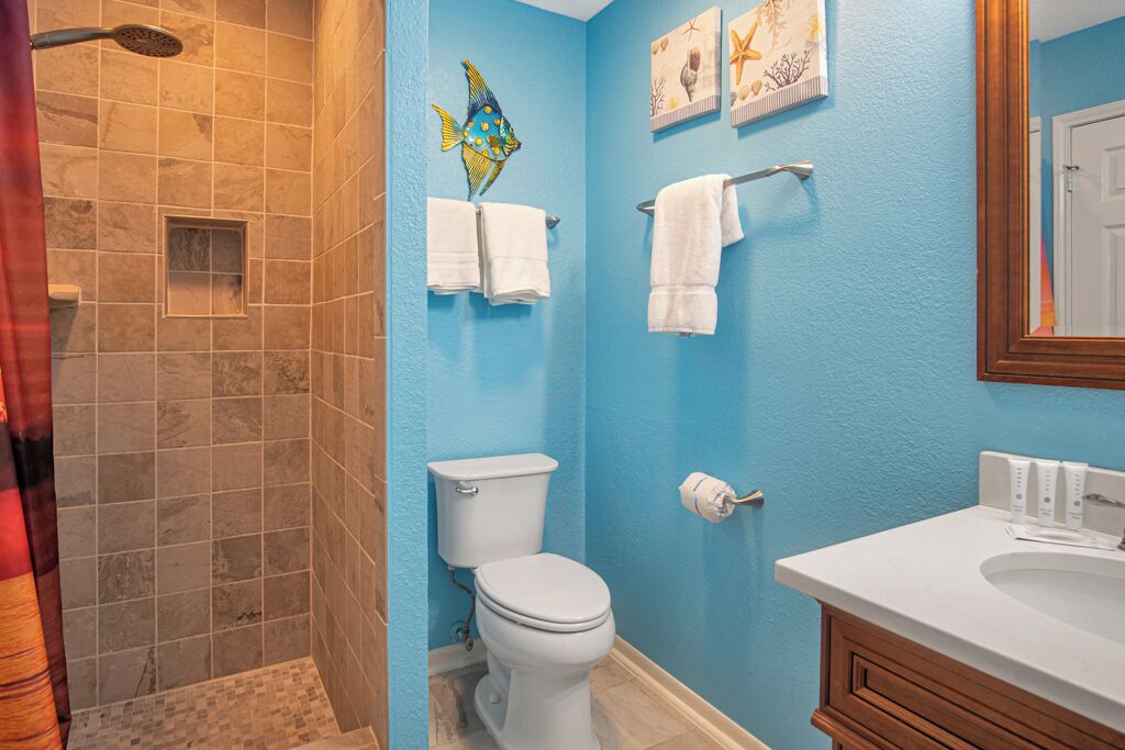 A bathroom with a blue wall, a white toilet, a shower area, and a sink with a wooden vanity.