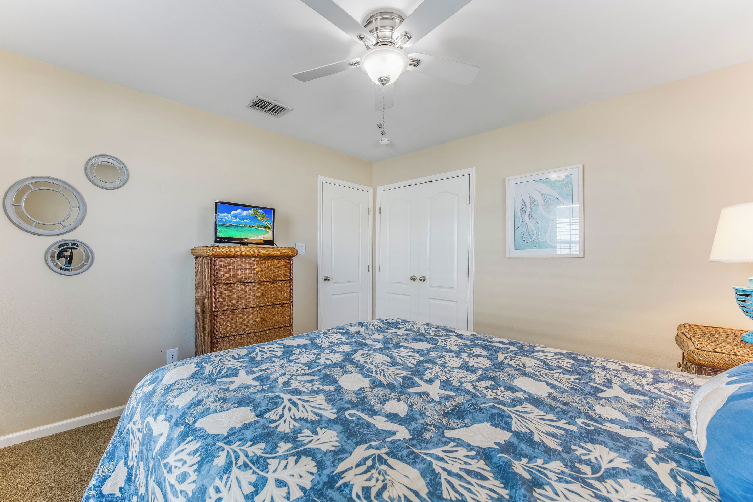A bedroom with a bed, a ceiling fan, a dresser, and two doors.
